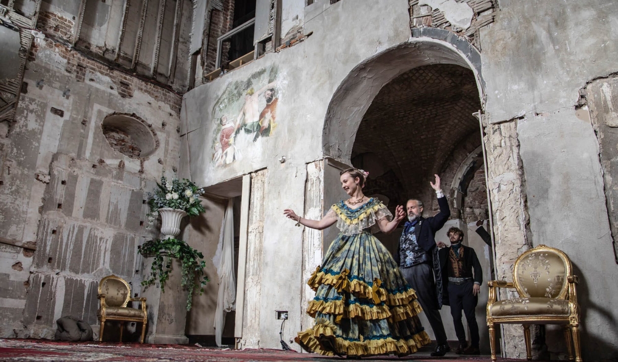 Scene from Opera Glassworks’ cinematic adaptation of Verdi’s “La Traviata.” A woman in a lavish 19th-century gown dances gracefully in a grand, decayi