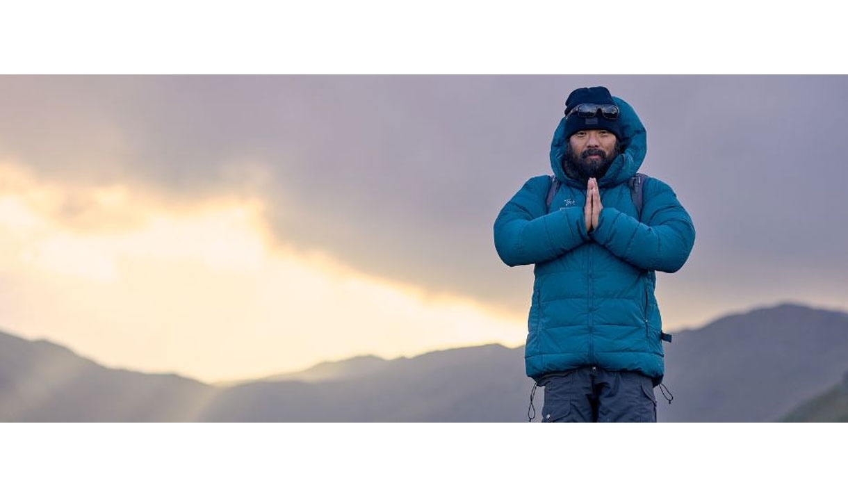 Krish Thapa poses atop a mountain with a sunrise in the background