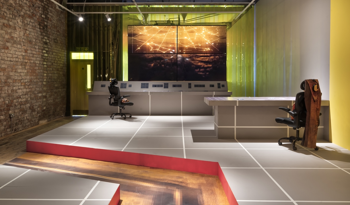 Installation view of Reactor by Felicity Hammond which depicts a control room with a film shown on 4 TV monitors. The still in this image shows conste