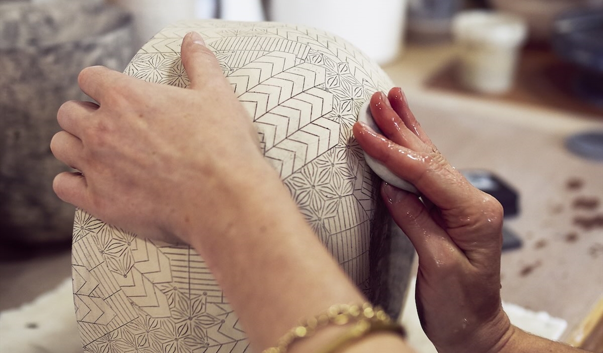 Frances Priests hands working on a large inscribed piece of her ceramic work
