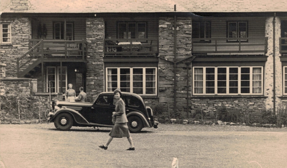 Gwyneth Alban Davis walking past a hotel with cars parked outside.