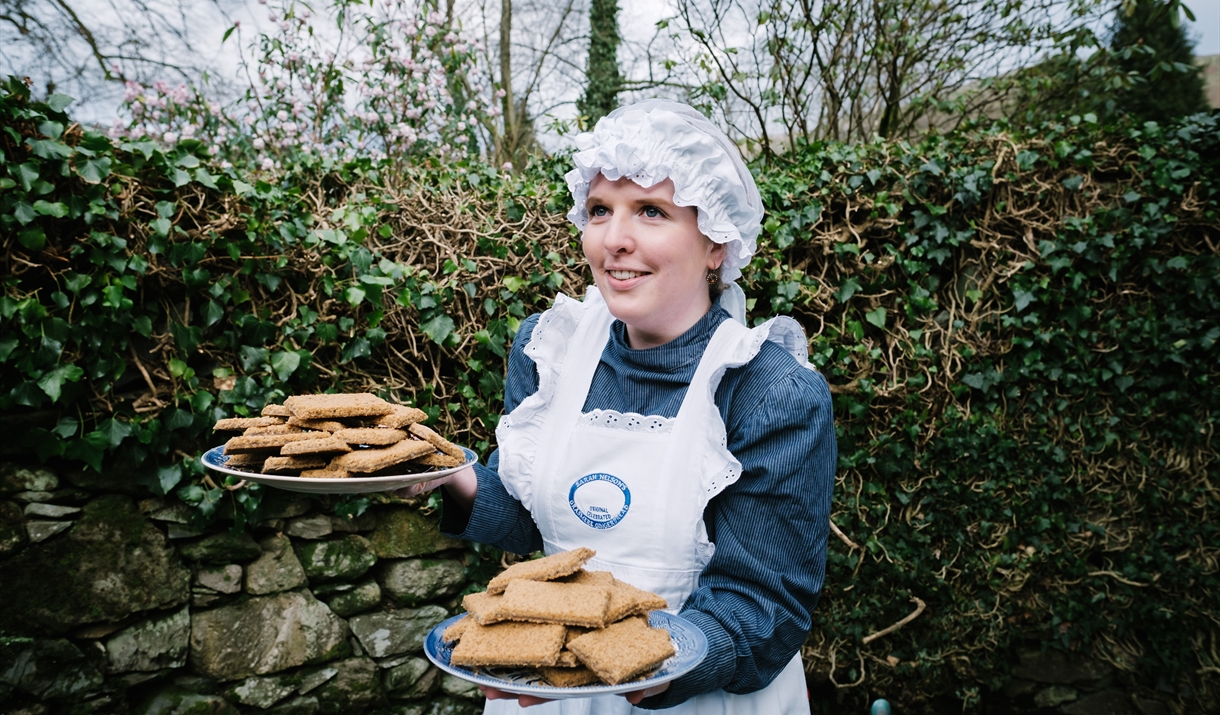 A staff member at Grasmere Gingerbread®. dressed in Victorian uniform holding a plate of freshly baked Grasmere Gingerbread