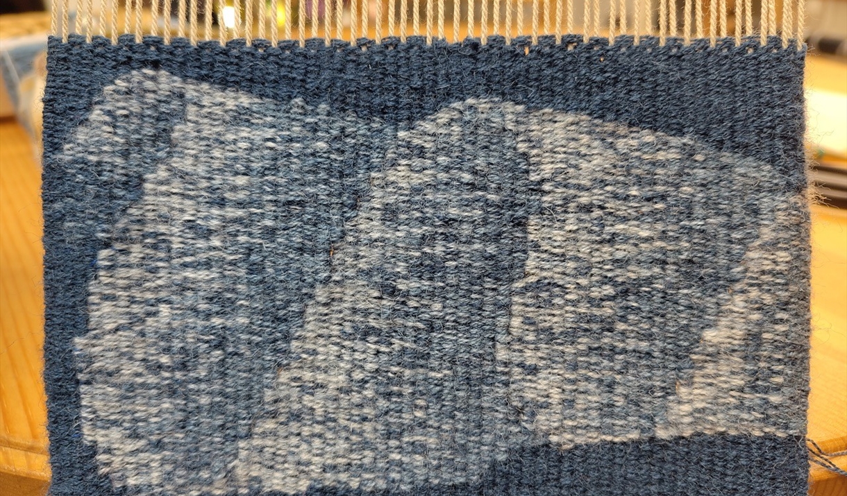 A blue and white woven textile displayed on a wooden table, showcasing intricate patterns and textures.