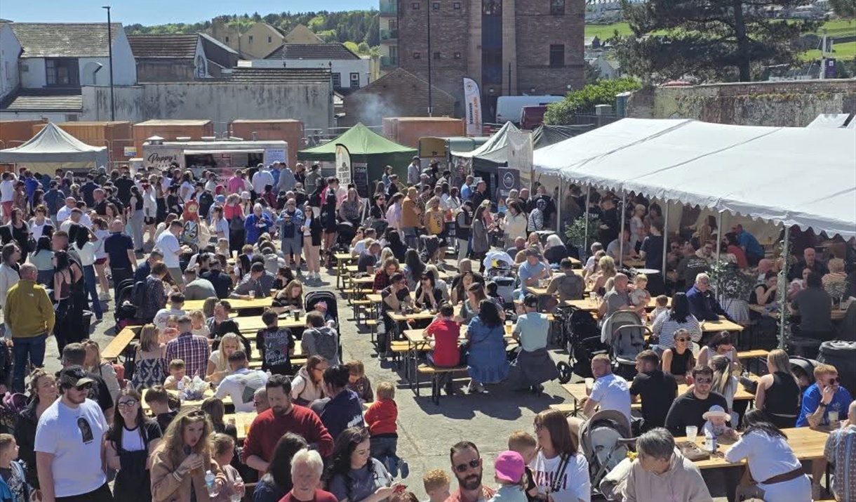 Eat Street Cumbria courtyard with people eating and drink, food vendors around the perimeter with a marquee and plenty of seating.