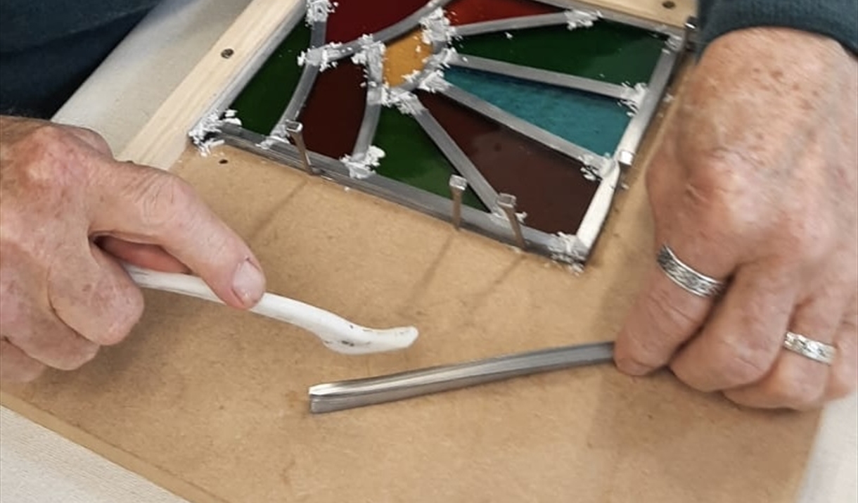 A man carefully cuts a piece of glass with a knife, demonstrating precision and focus in his task.