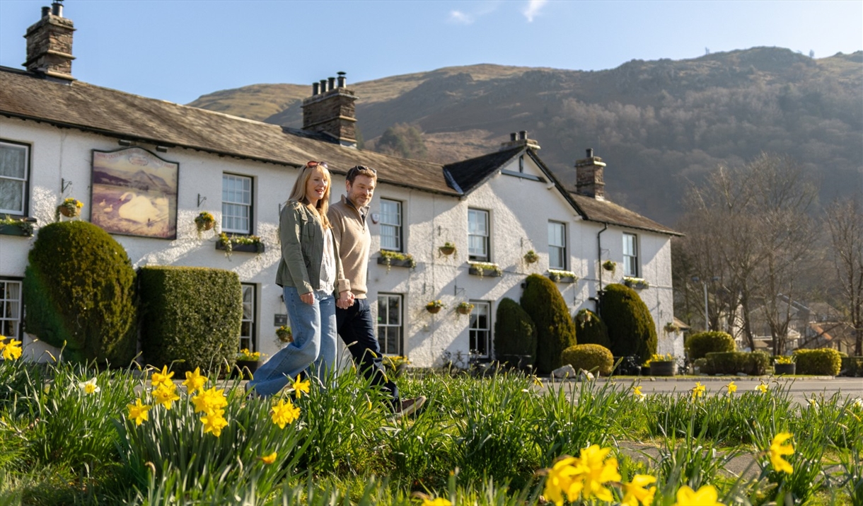 Couple walking with daffodils in front of The Swan at Grasmere in the Lake District, Cumbria