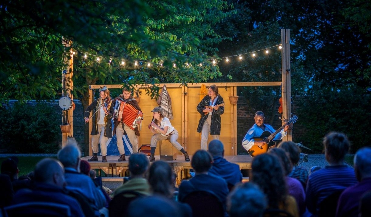 The Three Inch Fools performing on a stage at night in the gardens of Muncaster Castle