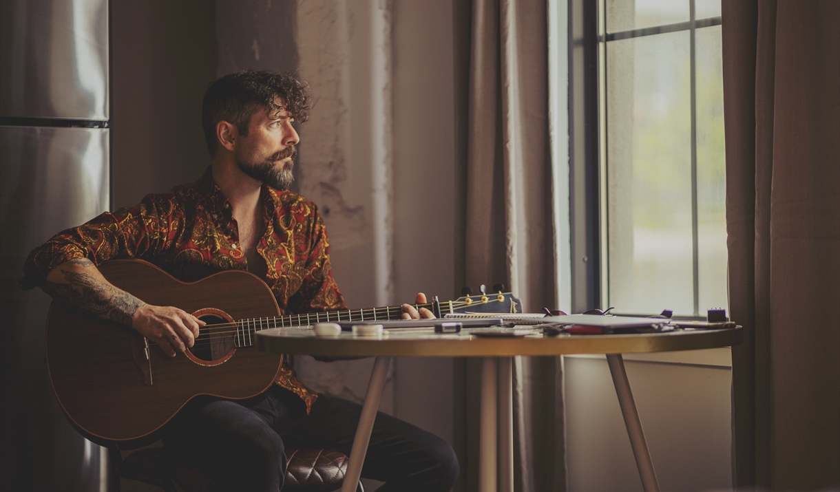 Niall McCabe holding a guitar while looking out a window
