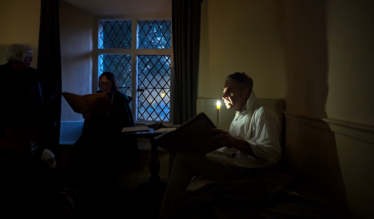 A dark room with a man reading stories by candlelight