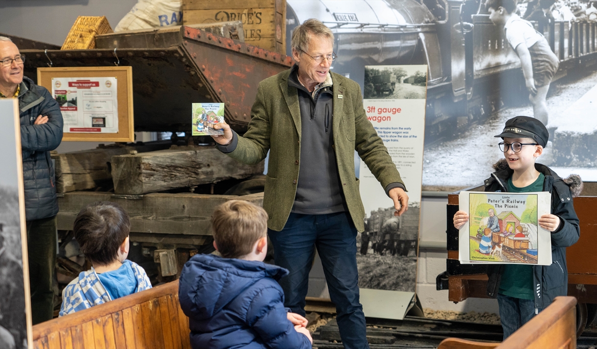 A man holding up a children's book to 3 children