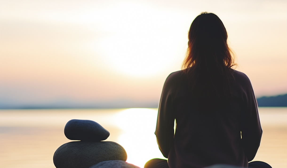 photo of a silhouetted person sat looking over the ocean