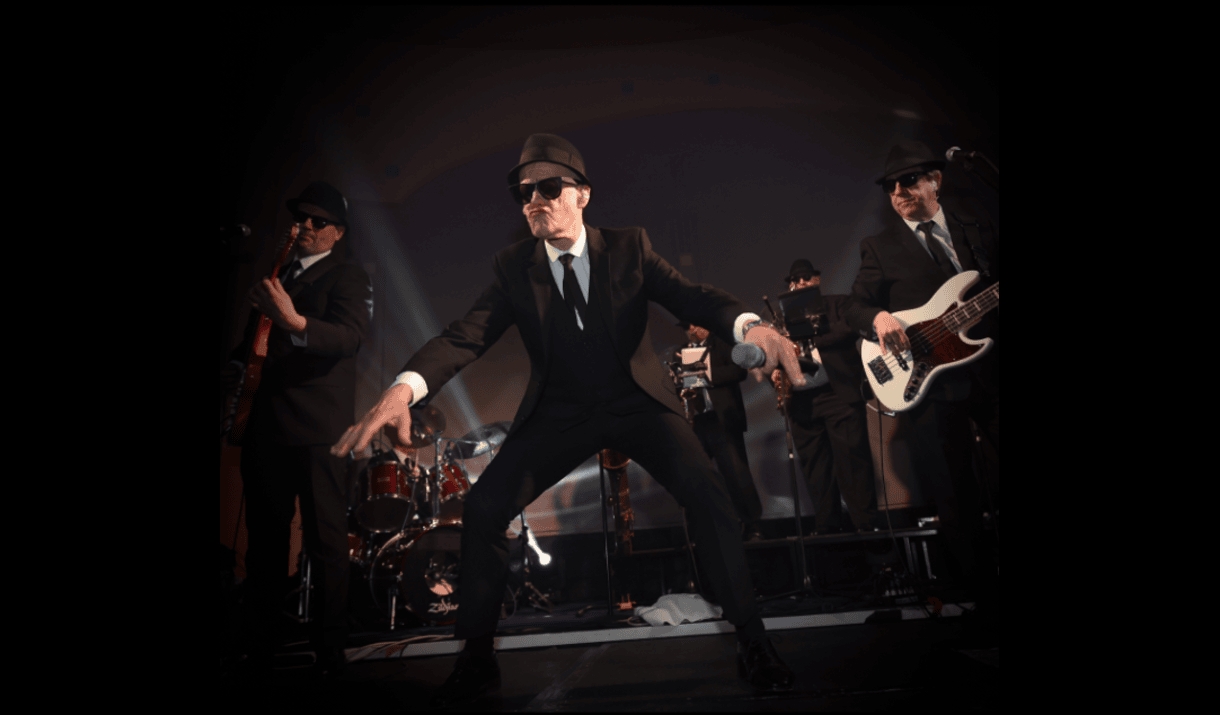 Photo of a soul band dressed in black suits with a lead singer guitarist and drummer