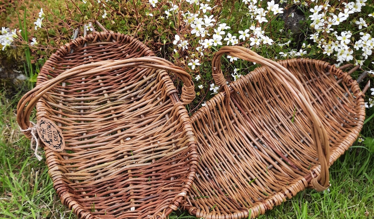 Two woven wicker baskets resting on a grassy surface, highlighting their rustic appearance.