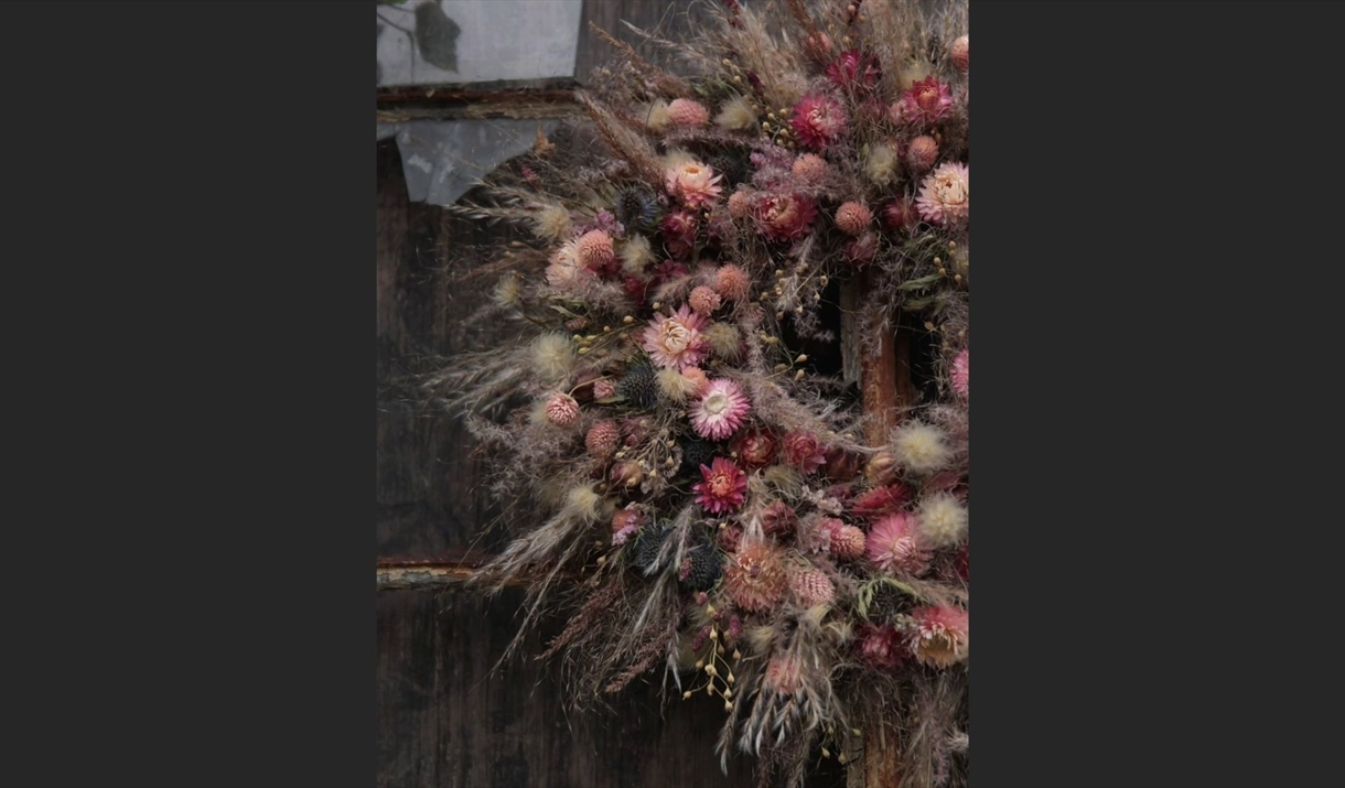 A decorative wreath made of dried flowers and leaves is hung on a rustic wooden door.