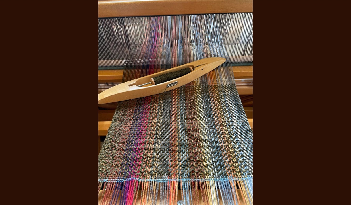 A weaving loom featuring a wooden shuttle resting on its surface, showcasing the textile creation process.