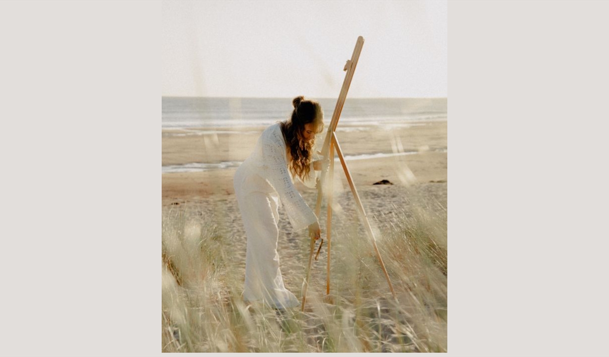 Women on the beach setting up an easel dressed in all white.