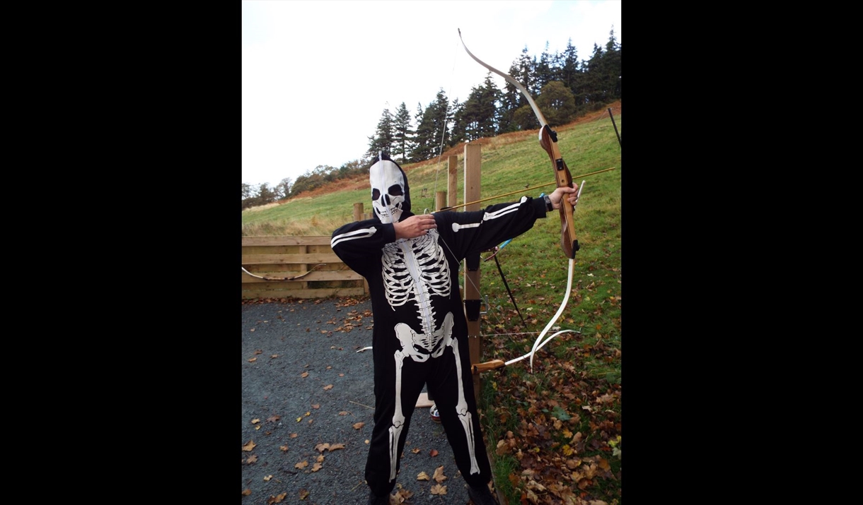 Person dressed as a skeleton drawing a bow and arrow in a field
