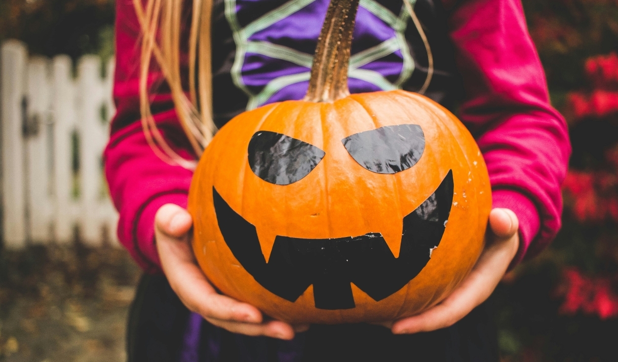 A girl holding a pumpkin with a face drawn on it