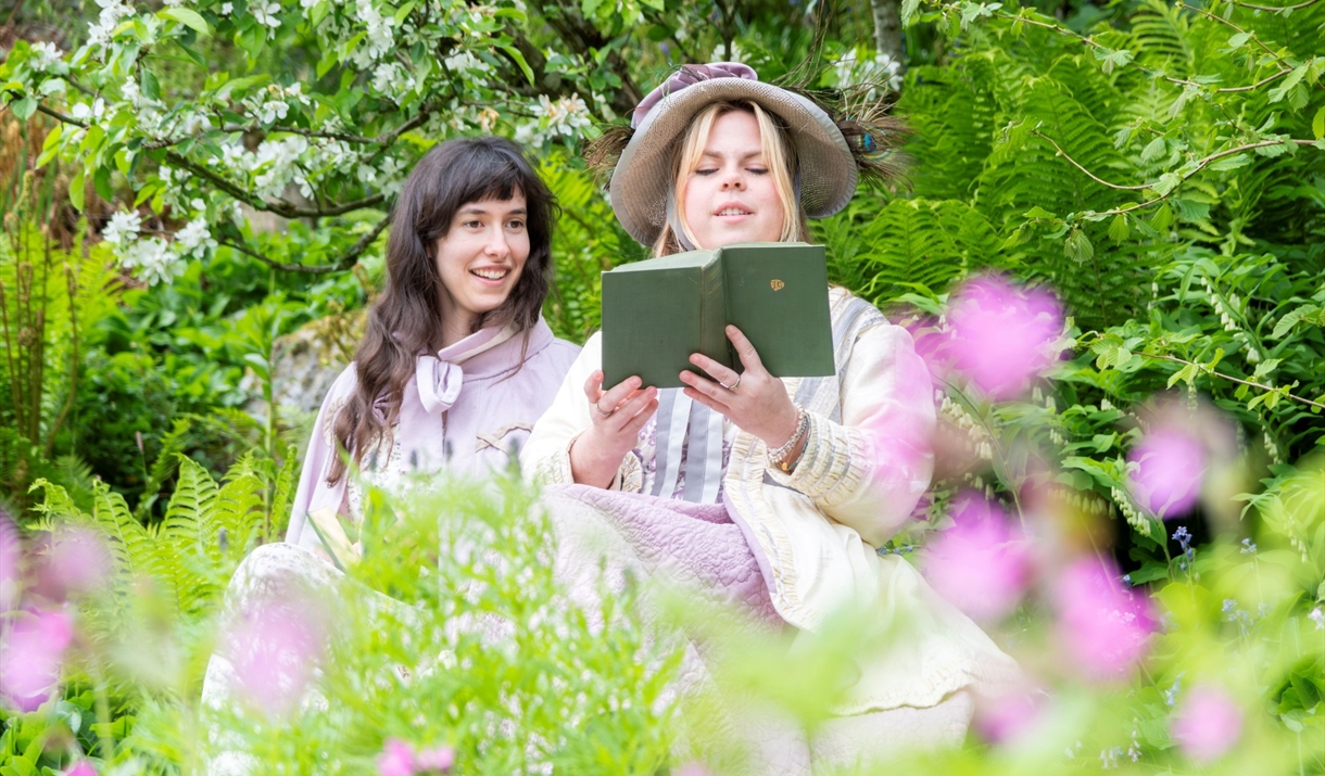 Photograph of two women in regency costume reading books in a garden.