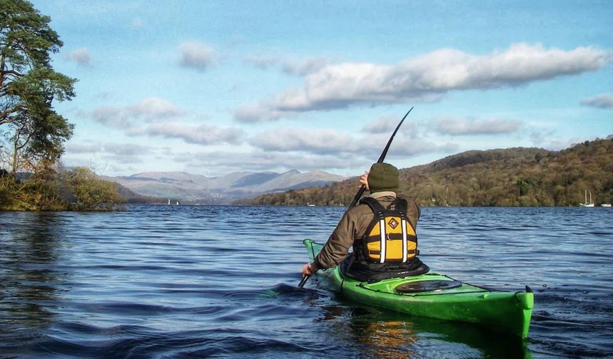 Person happily kayaking across Windermere during a Guided Paddle Tour by Windermere Canoe Kayak on a bright sunny day