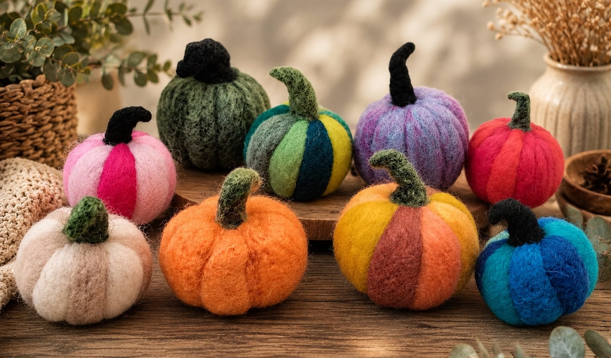 A collection of vibrant felt pumpkins arranged on a table, showcasing various colors and sizes.