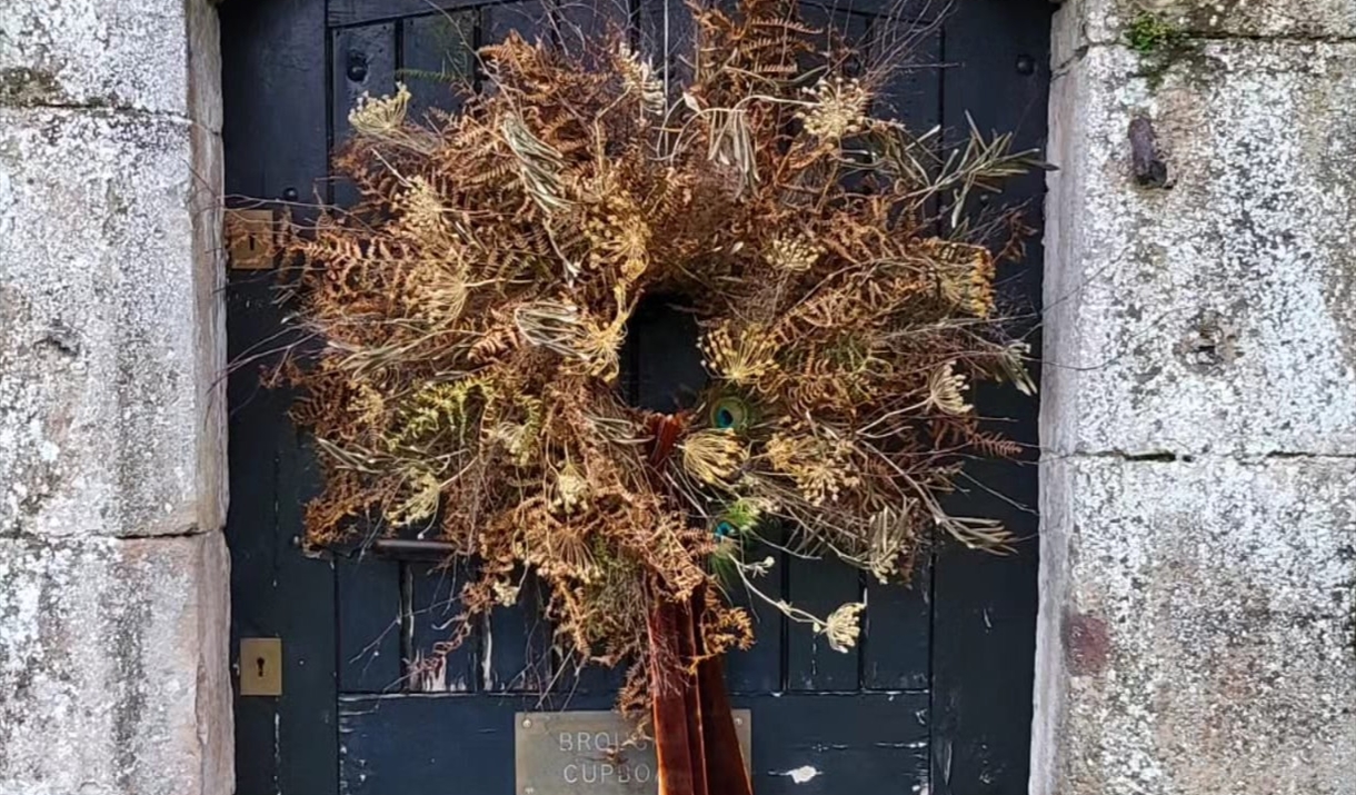 A decorative wreath adorned with a large bow, hanging on a wooden door.