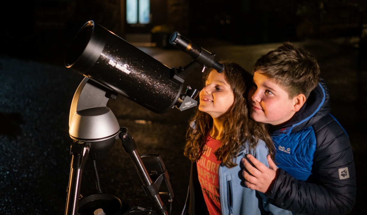 Brother and sister looking through a large telescope together at night