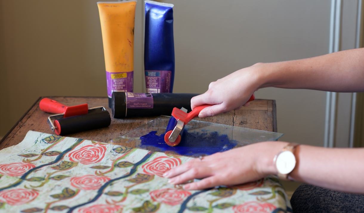 Person holding roller over ink next to printed patterned fabric