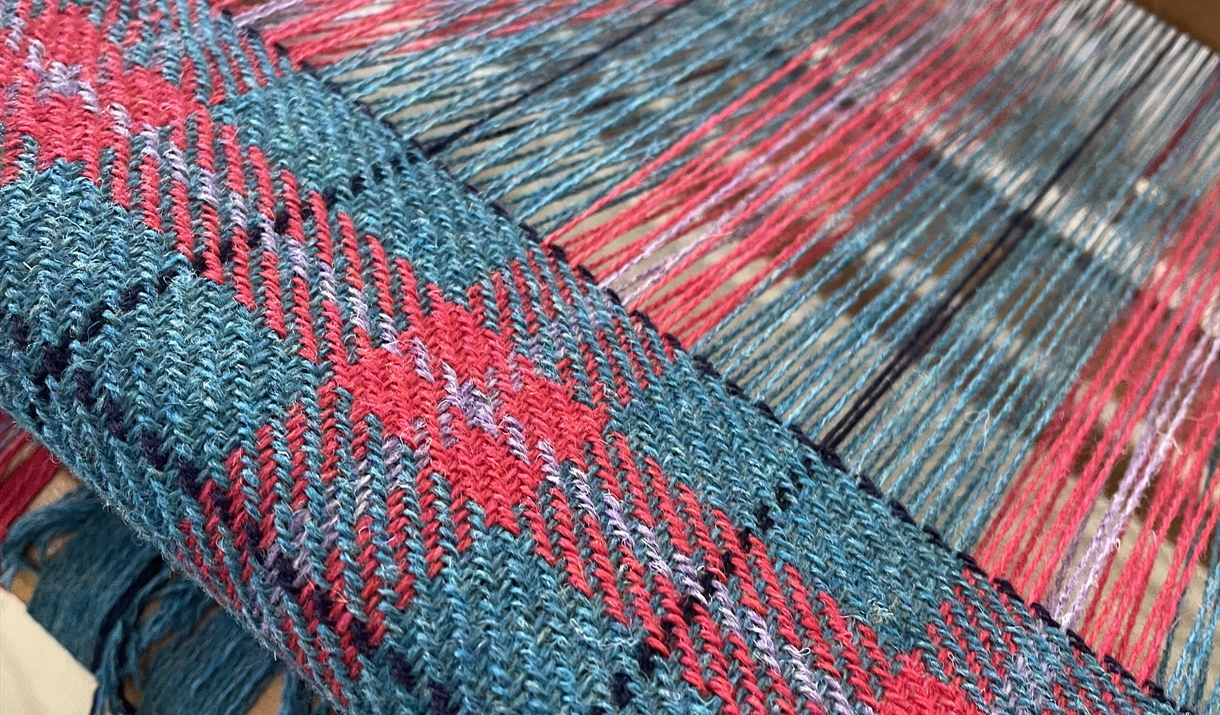 A blue and red plaid weaving loom displaying a vibrant red and blue pattern in progress.