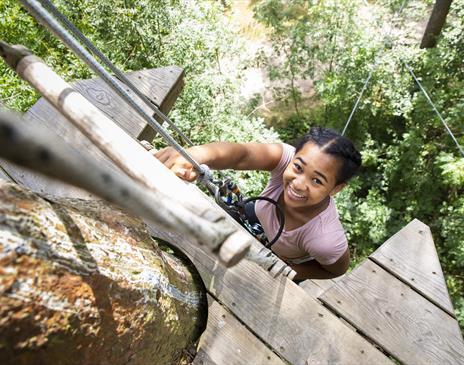 a smiling child climbing up a ladder on a high rise rope course