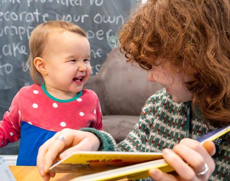 A kid laughing at an adult who is reading them a book