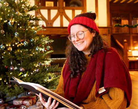 Women smiling while reading a book by a Christmas tree