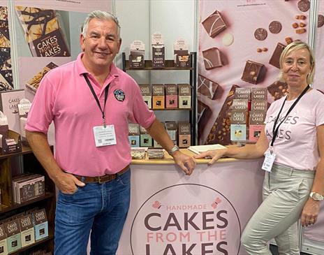 Owners of Cakes From The Lakes pose in pink t-shirts at a stand with cakes and treats