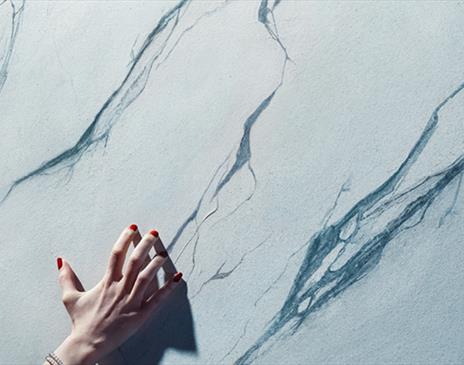 hand with red nail polish brushing against a marble wall