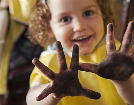 Smiling child holding up hands covered in dirt, showing them proudly