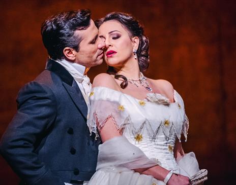 A man stood closely behind a women with the women leaning back looking in a romantic manner