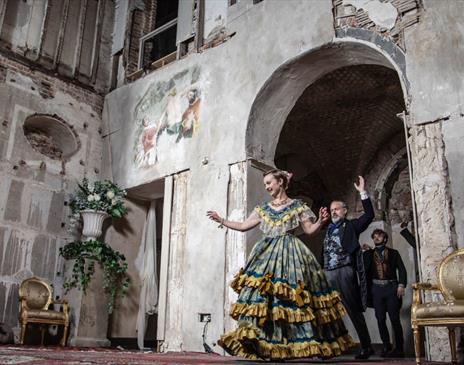 Scene from Opera Glassworks’ cinematic adaptation of Verdi’s “La Traviata.” A woman in a lavish 19th-century gown dances gracefully in a grand, decayi