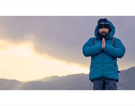 Krish Thapa poses atop a mountain with a sunrise in the background