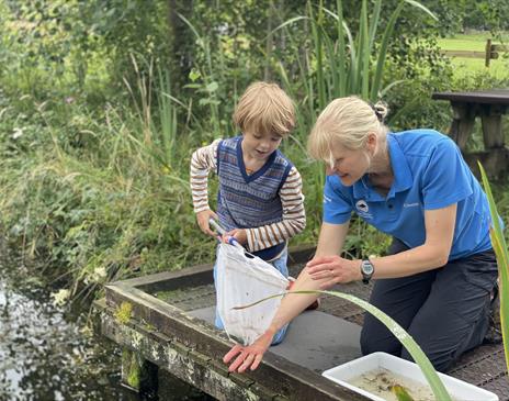 A boy holding a net next to a pond with a women who is helping