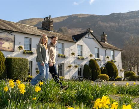 Couple walking with daffodils in front of The Swan at Grasmere in the Lake District, Cumbria