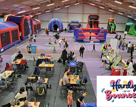 Indoor family fun event with large inflatable obstacle courses, bouncy castles, slides, and activity areas. Children and parents are playing, while ot