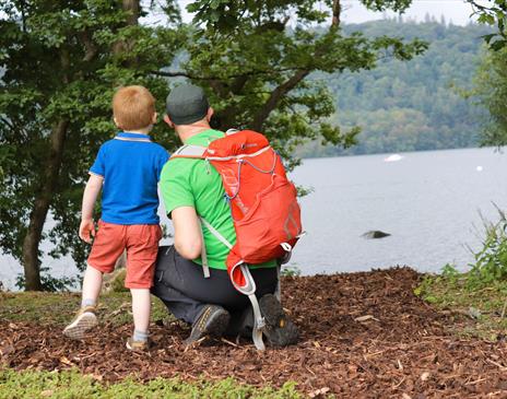 a child and an adult (wearing hiking gear and a backpack) looking over a lake