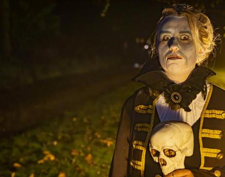 Women in white make up holding a human skull stood in a field lit by candlelight