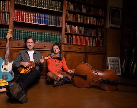 Band members sitting on the floor in a library holding ukulele