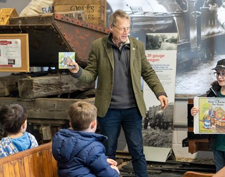 A man holding up a children's book to 3 children