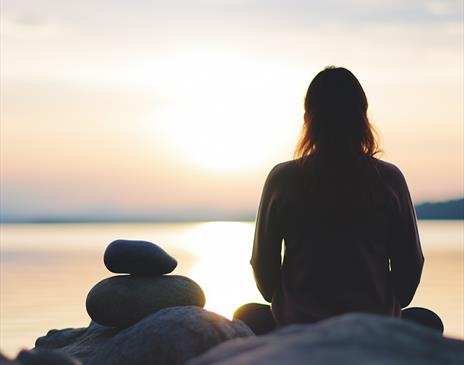 photo of a silhouetted person sat looking over the ocean