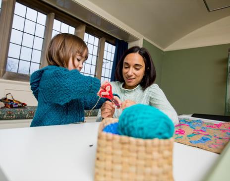 A child and a female adult doing arts and crafts with some wool