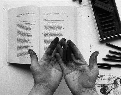 Black and white photo of dirty palms hovering above a table with a book and pencils