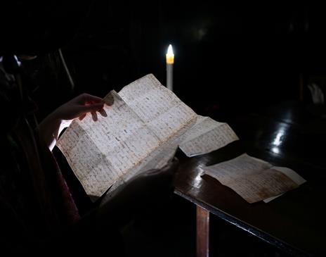 a person reading a page of Mary Shelley's Frankenstein in a dark room only visible by candlelight