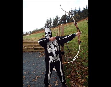 Person dressed as a skeleton drawing a bow and arrow in a field